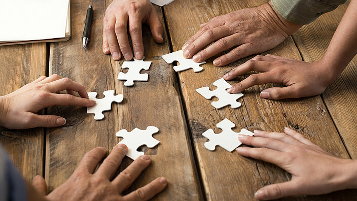 Hände die gemeinsam Puzzleteile zusammenfügen